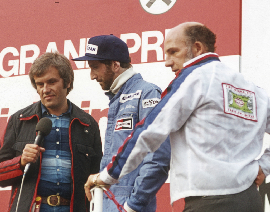 A youthful Helmut Zwickl, left, interviews John Watson who had just won the 1976 Austrian Grand Prix in his Penske whilst Stirling Moss looks on. ( Photo Peter Nygaard Grand Prix Photo)